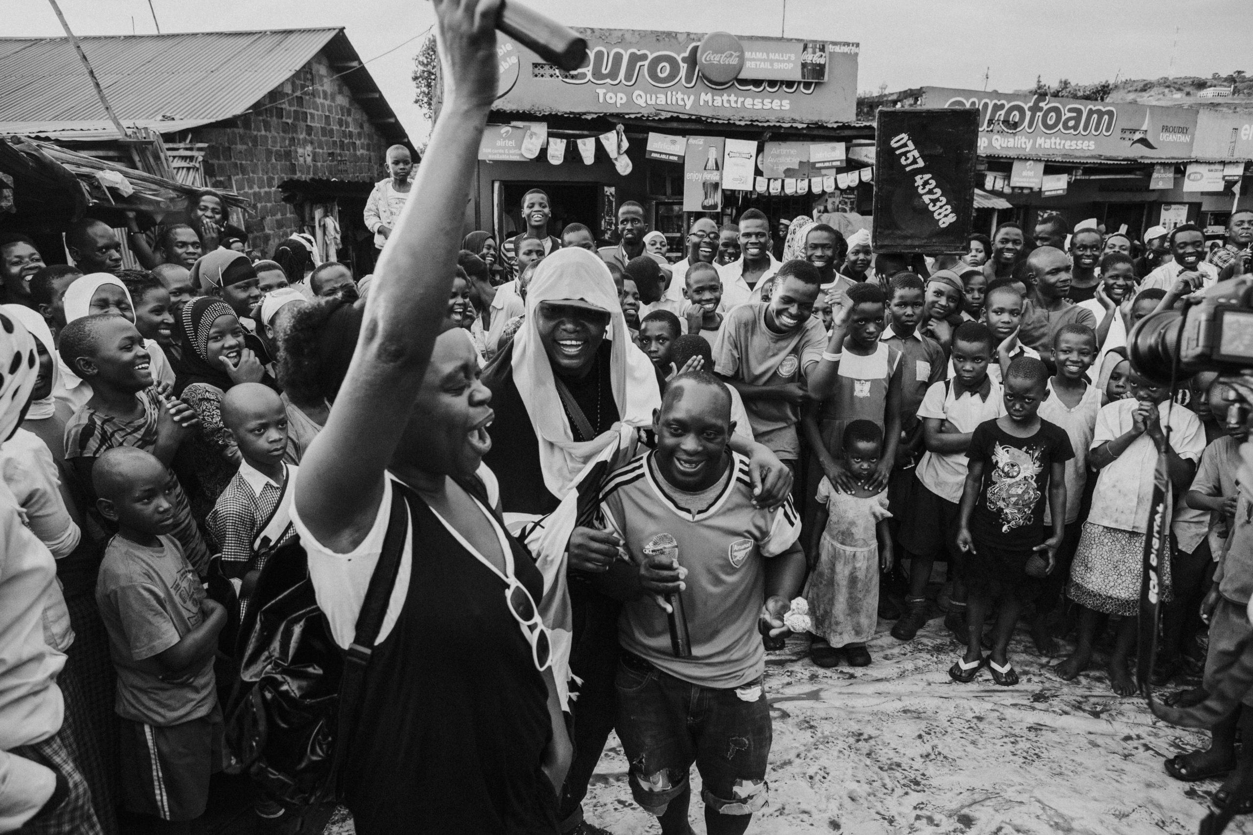 A performer holding a microphone before an outdoor community crowd